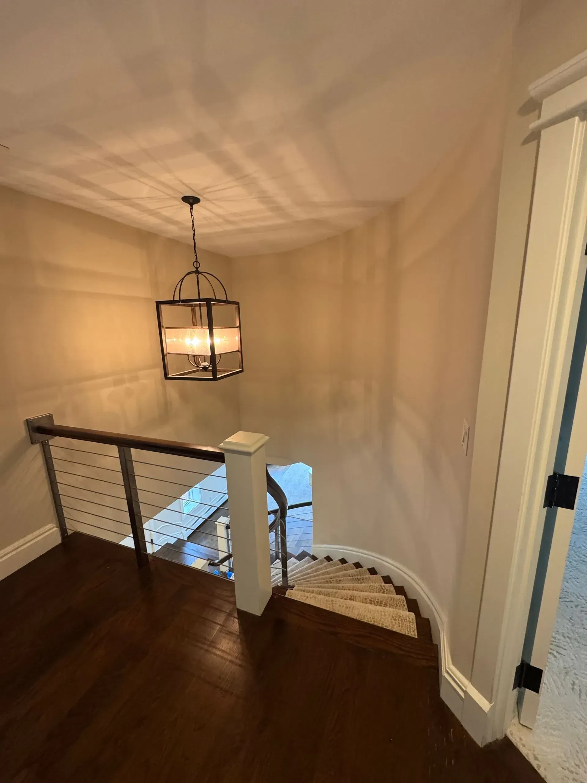 Stair landing with dark wood floor, white walls, and hanging lantern above a curved railing.