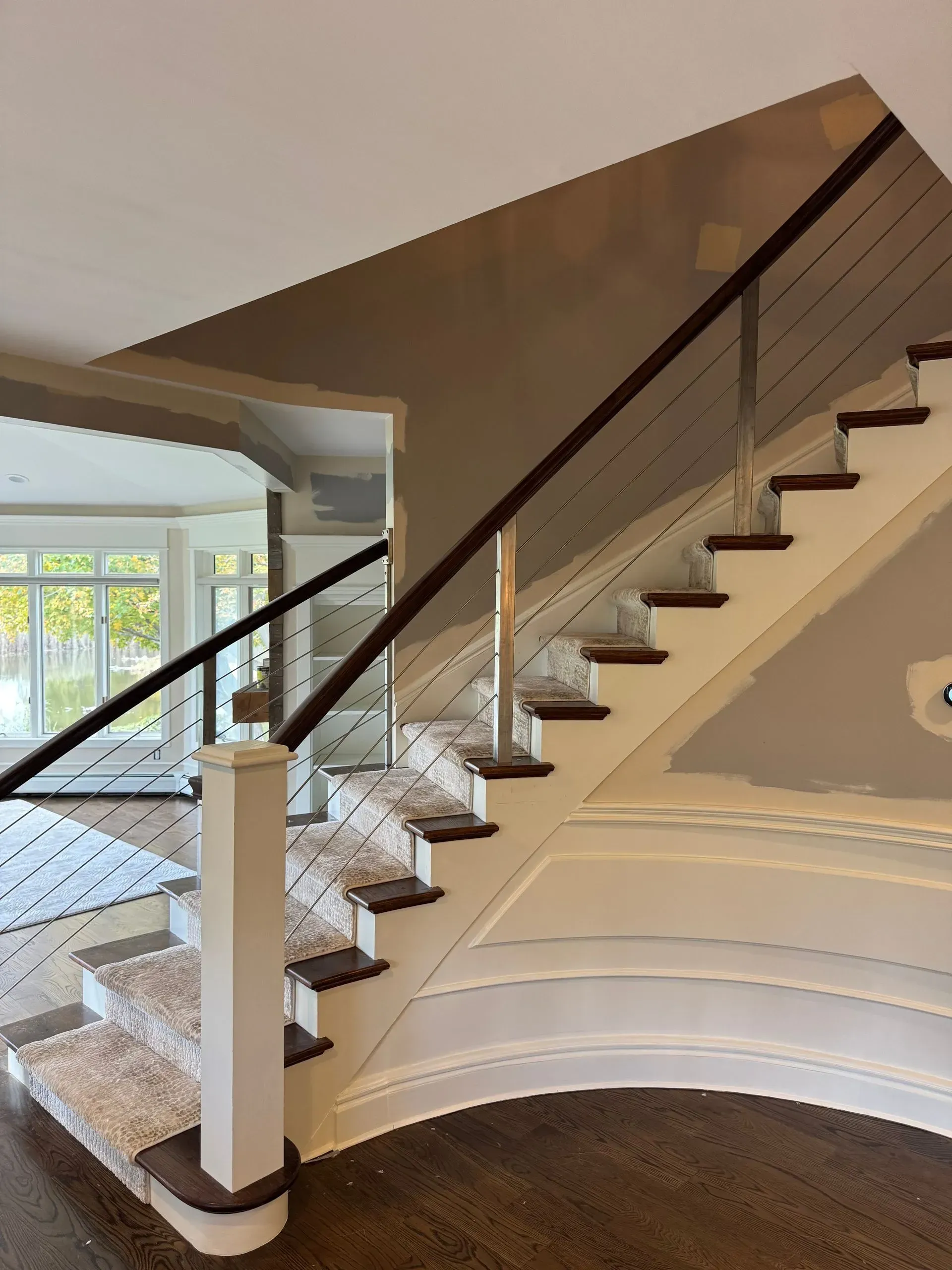 Curved indoor staircase with carpeted steps, dark handrail, and white banister in a bright home foyer
