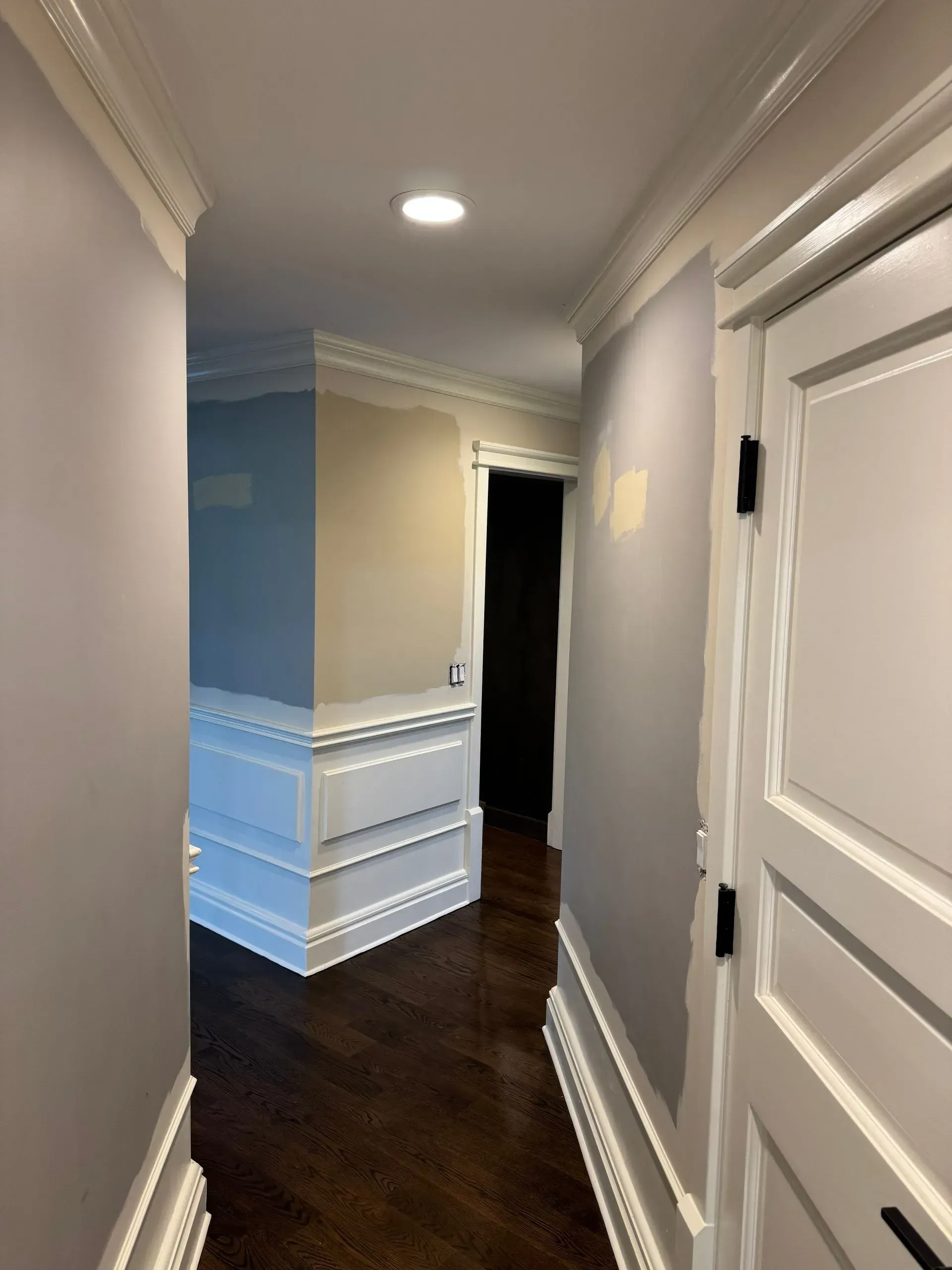 Narrow hallway with white wainscoting, dark hardwood floors, recessed lights, and open doorway ahead