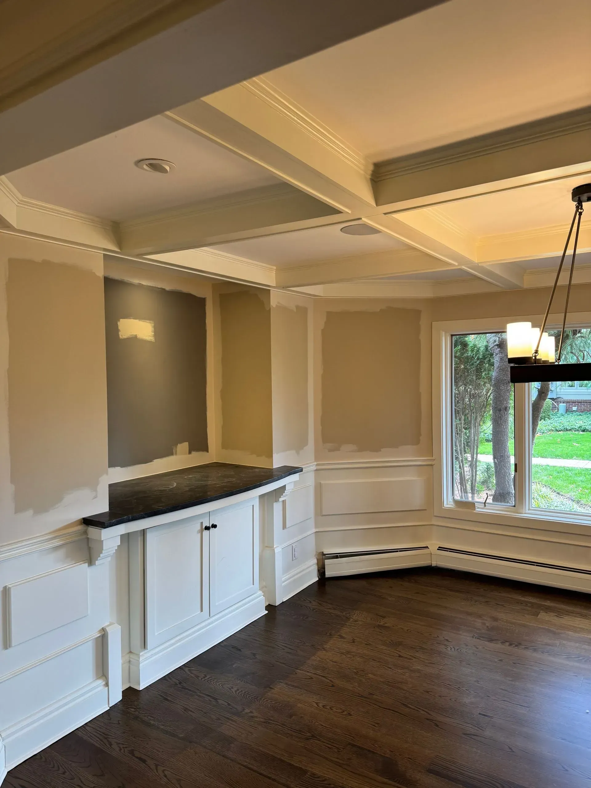 Empty dining room with dark hardwood floors, white wainscoting, coffered ceiling, and a large window.