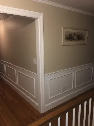Hallway with beige walls, white wainscoting, hardwood floors, and a framed picture on the wall