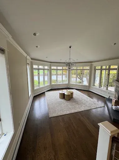 Bright sunroom with bay windows, dark wood floors, white rug, and a chandelier.