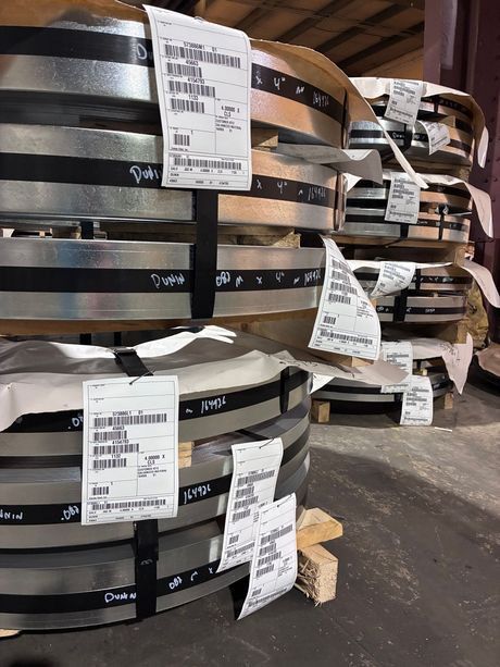 Stacks of black metal coils with white labels in an industrial warehouse