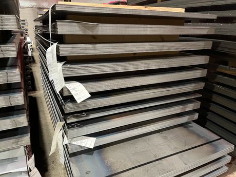Stacks of metal shelving panels in a warehouse aisle, with tags attached to the front pieces.