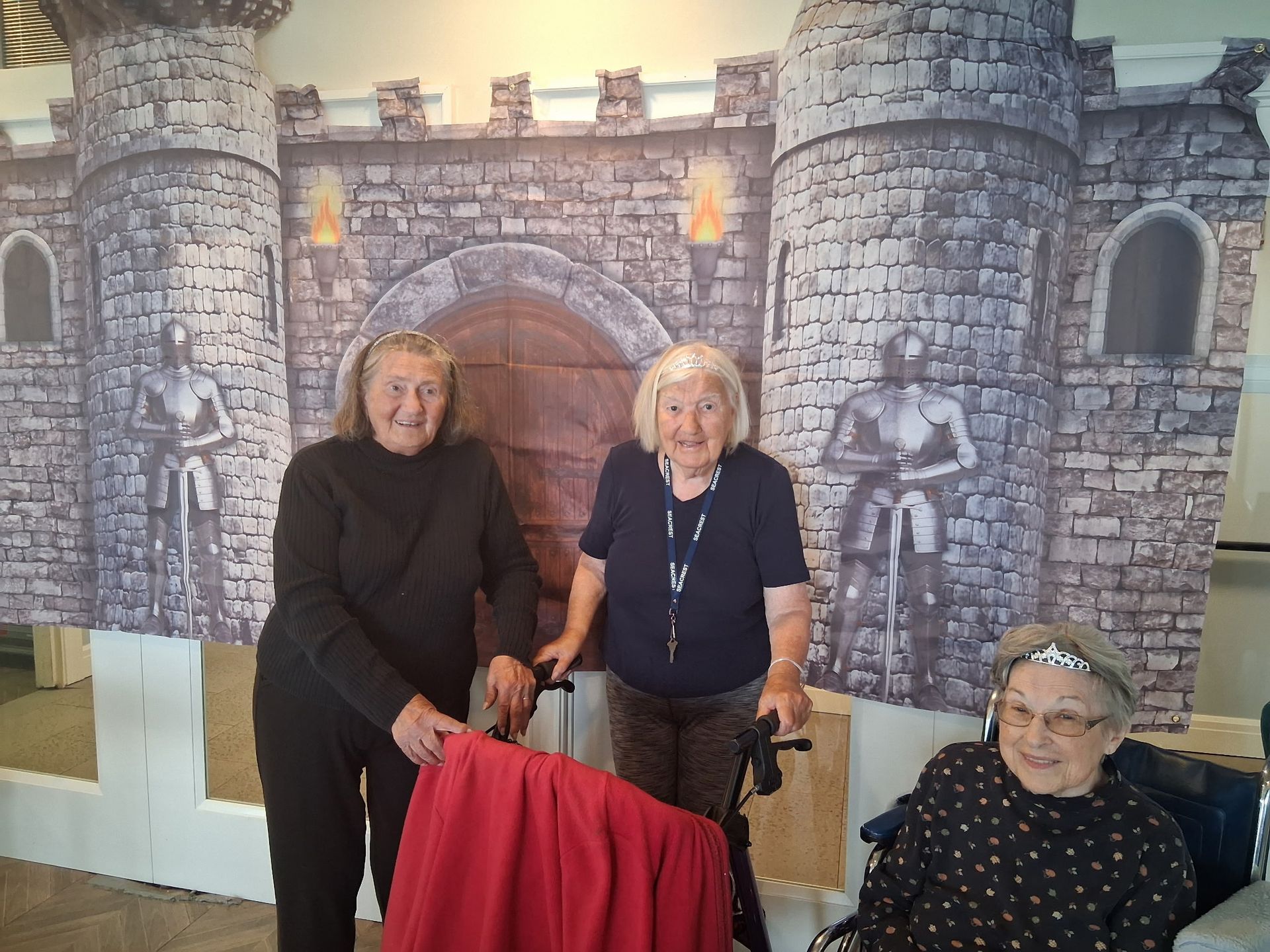 Three people posing before a stone castle backdrop, with a red chair in front.