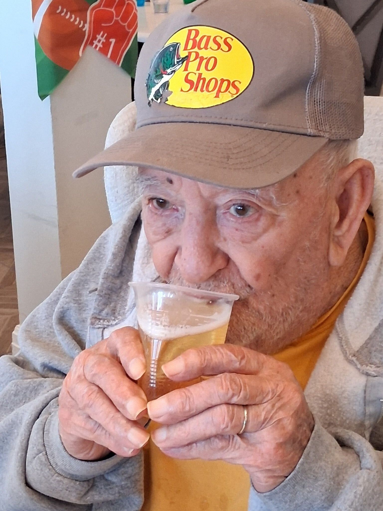 Man in tan cap sipping a glass of beer indoors