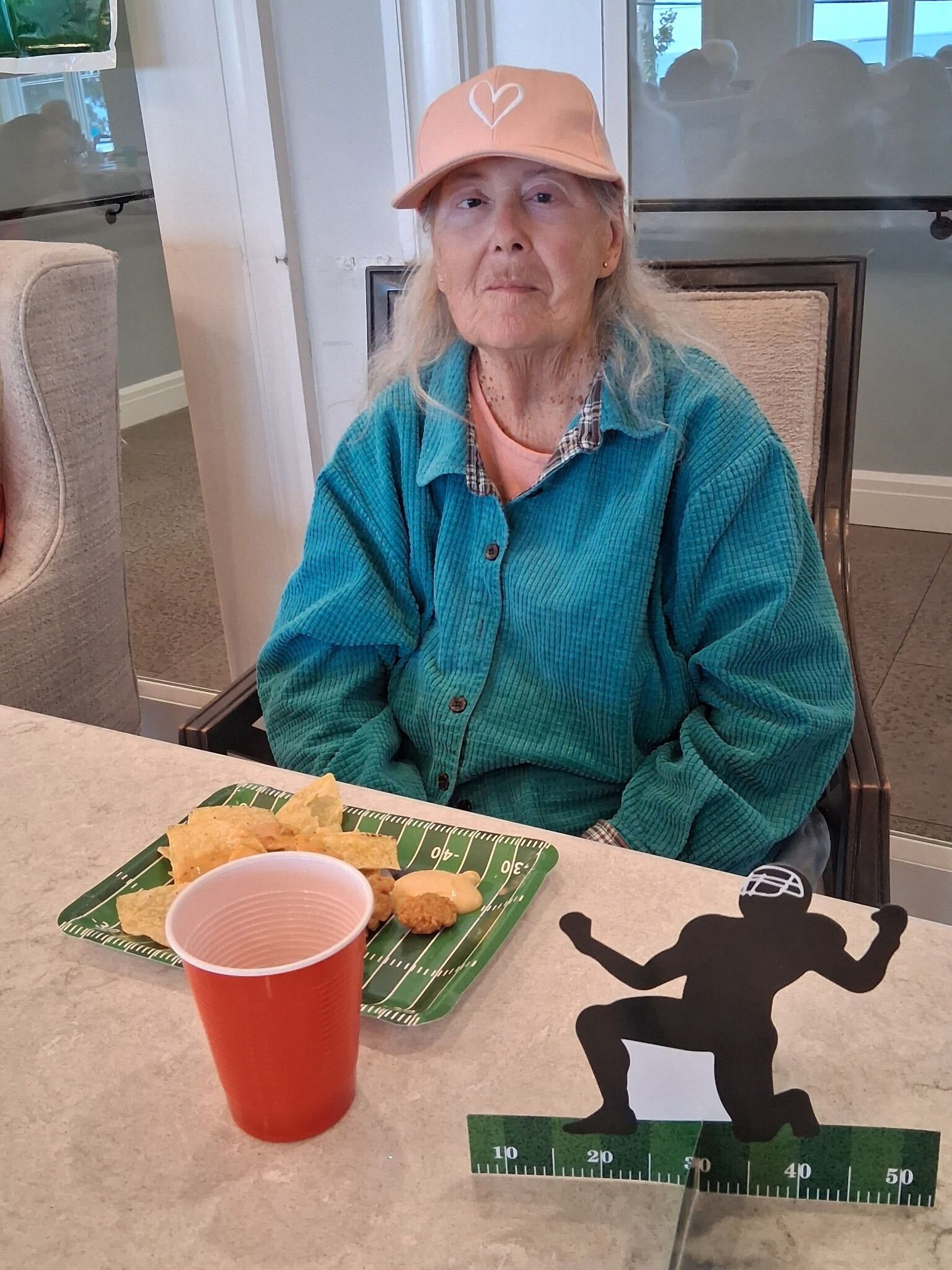 Woman seated at a table with a meal tray, red cup, and black silhouette decoration in a bright room