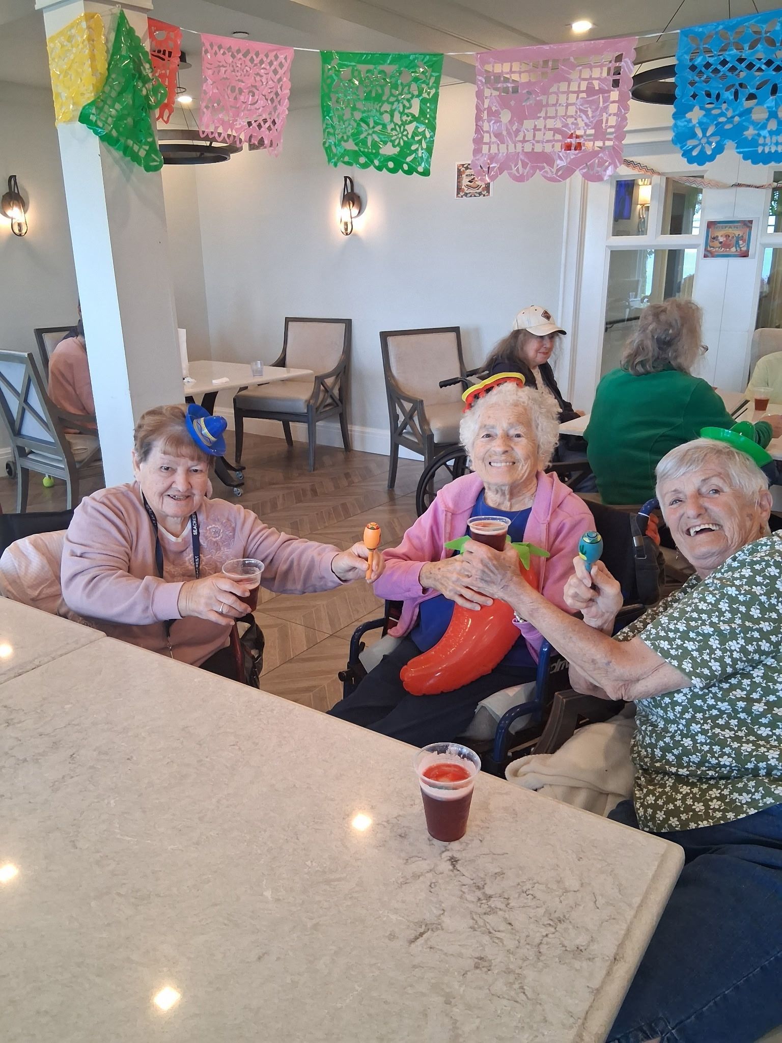 People in a bright room holding balloons at a festive table, with colorful paper decorations overhead