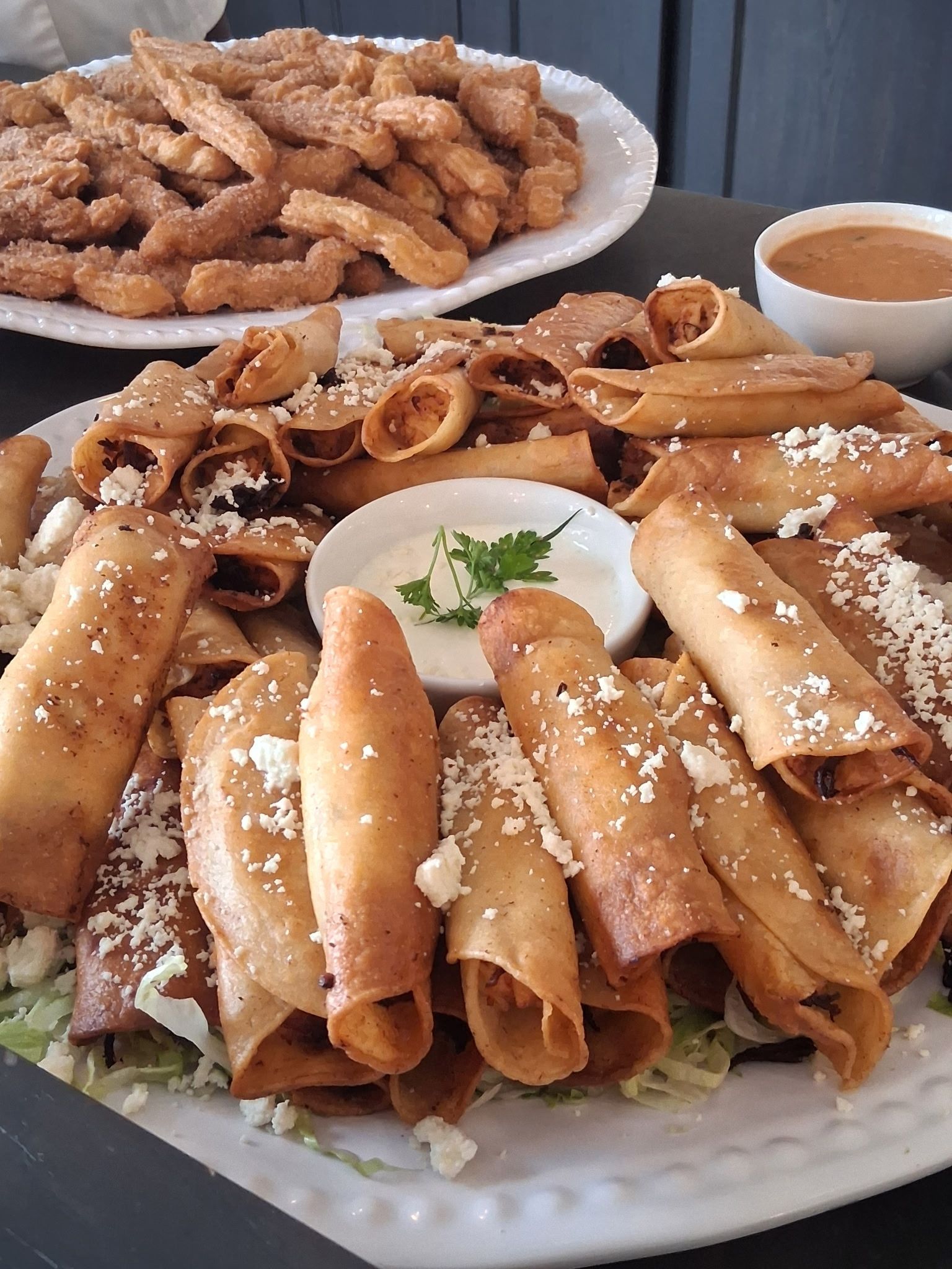 Plate of rolled crepes and pastries topped with powdered sugar, with a bowl of dipping sauce behind them.