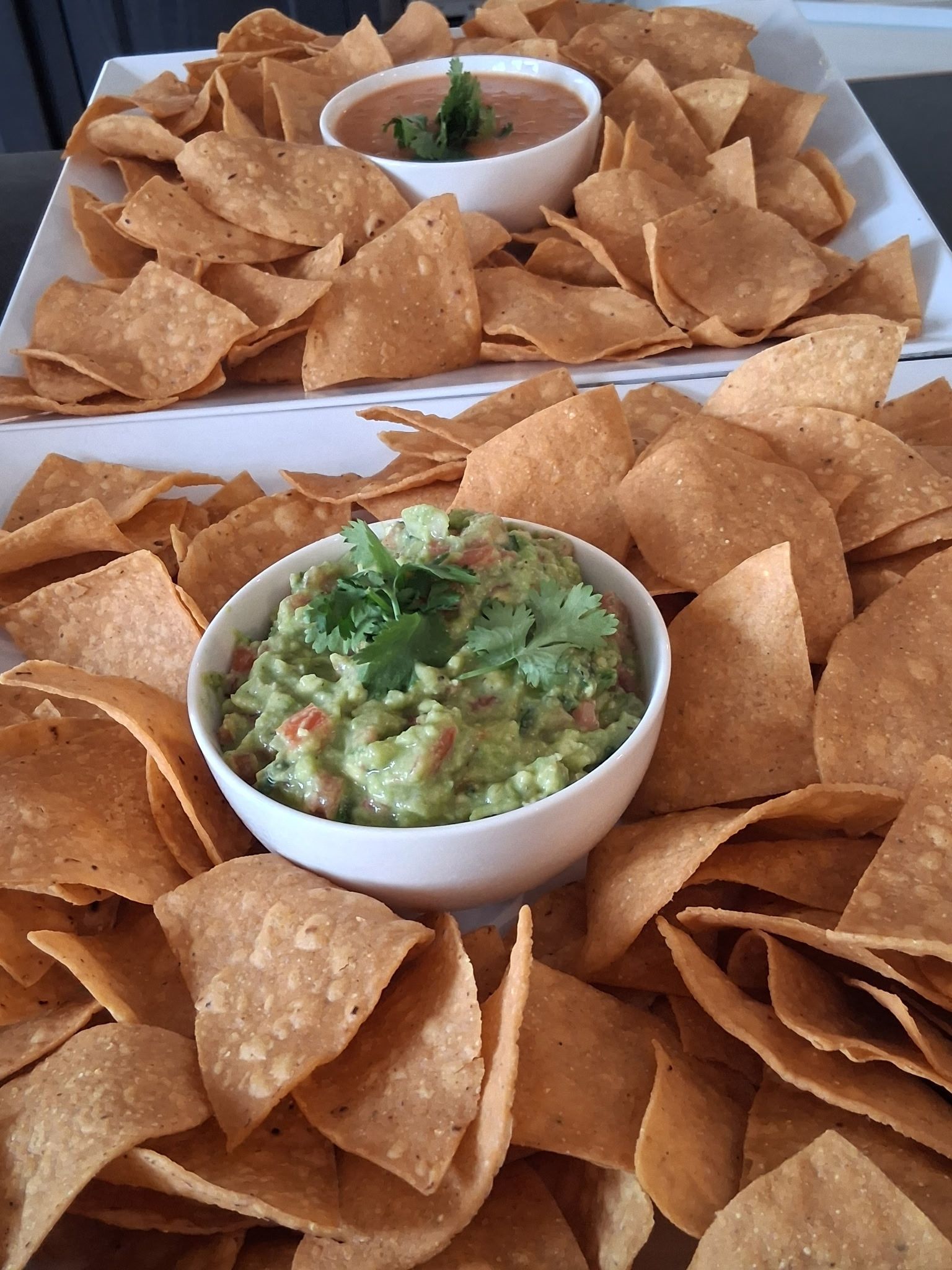 Bowls of guacamole and salsa surrounded by tortilla chips on a tray