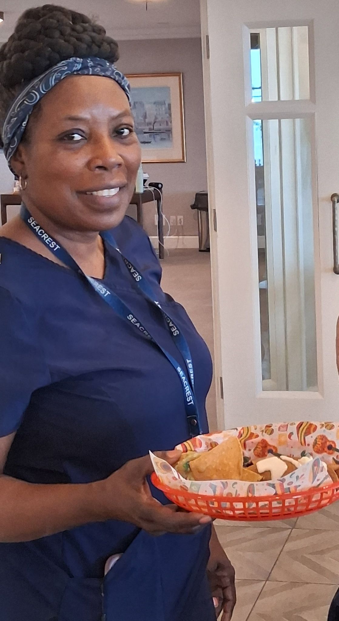 Woman in a blue shirt holding a tray of wrapped snacks indoors.