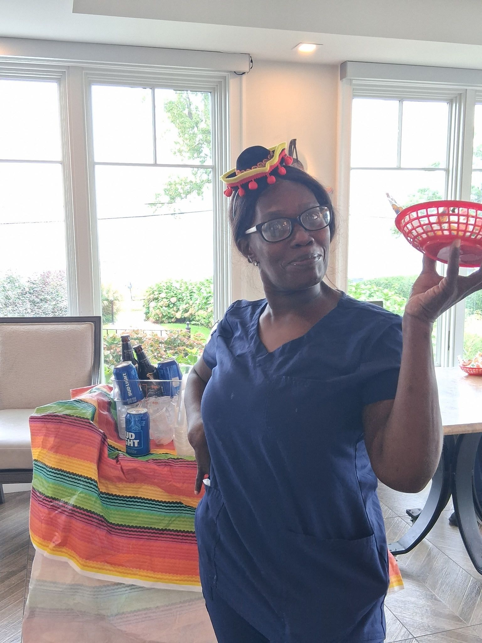 Person in navy shirt holding a red colander in a bright room with windows and colorful fabric behind them