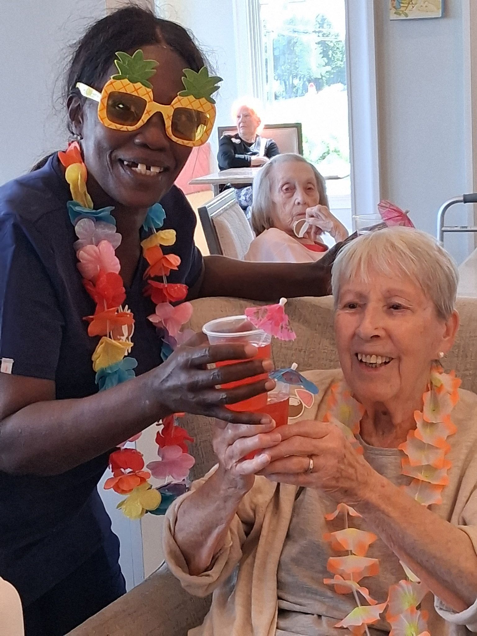 Caregiver handing a drink to a smiling resident during a festive activity in a care home