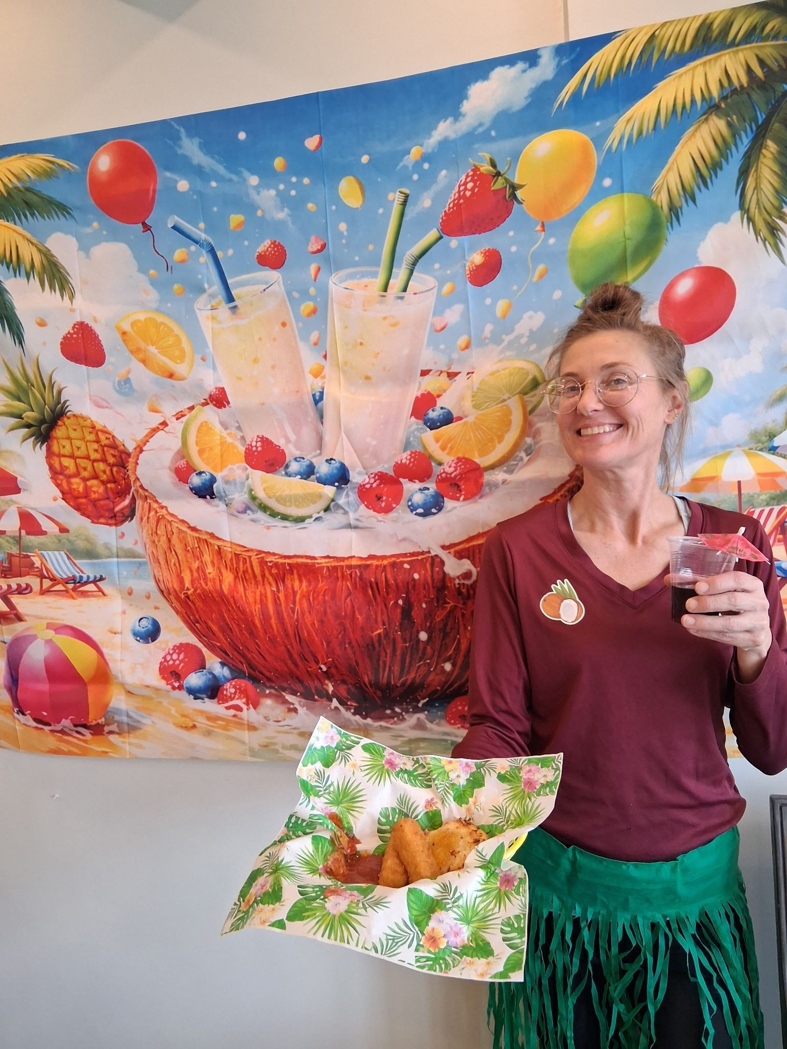 Smiling woman holding a drink in front of a colorful tropical fruit mural