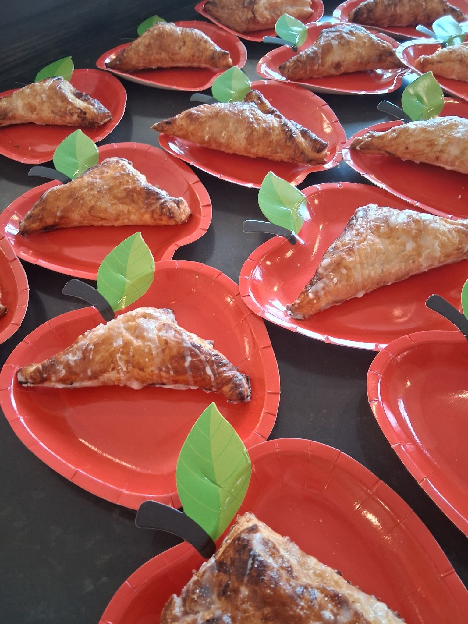 Red trays with triangular pastries topped with nuts, each garnished with a green leaf, arranged in rows
