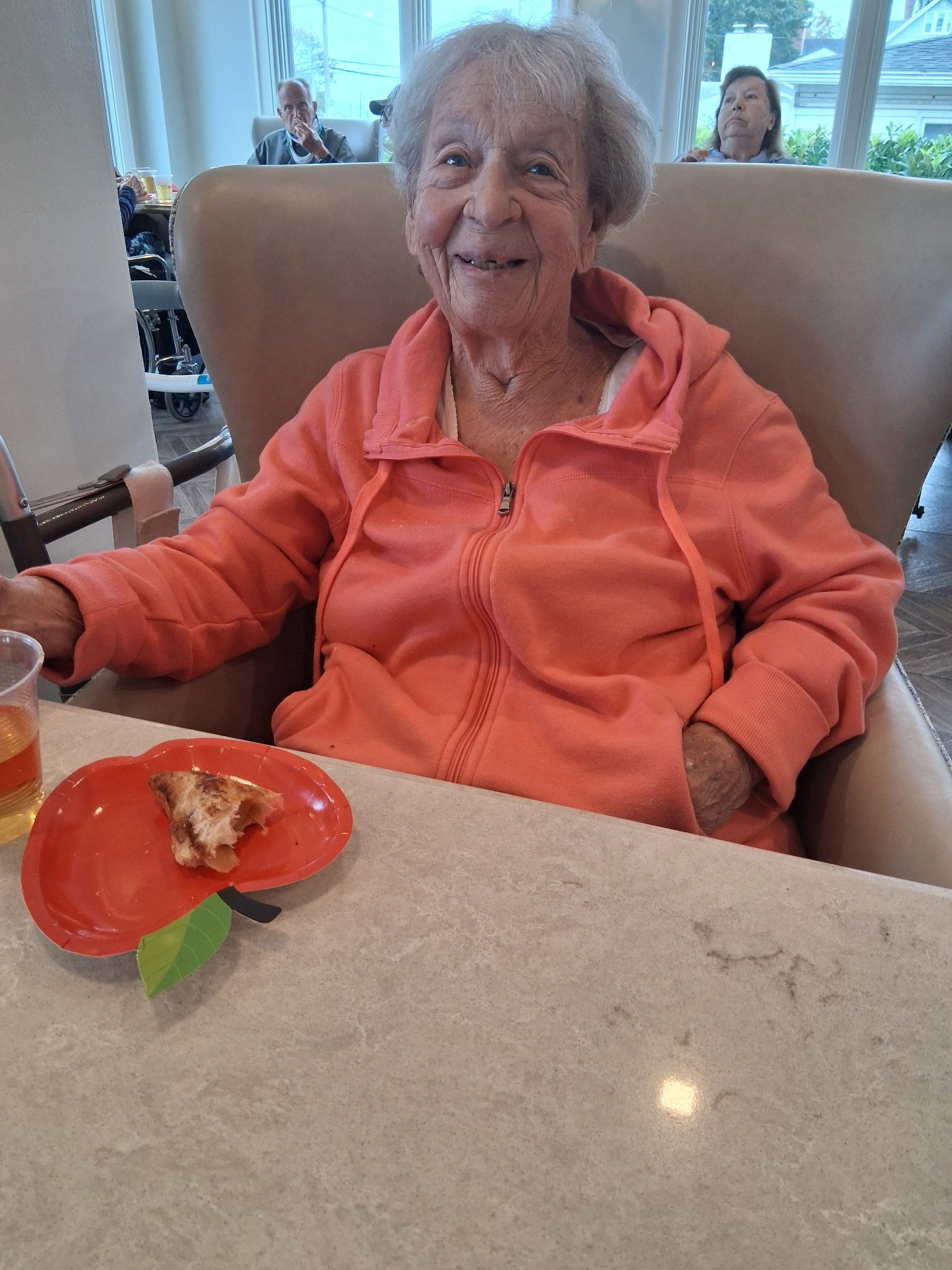 Smiling person in coral hoodie sitting at a table with a plate of cake in a dining room.