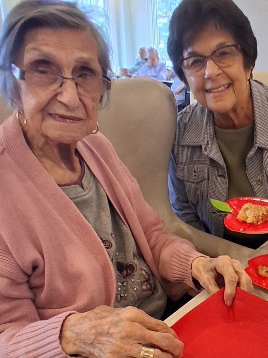 Two smiling people seated at a table, holding red trays in a bright room.