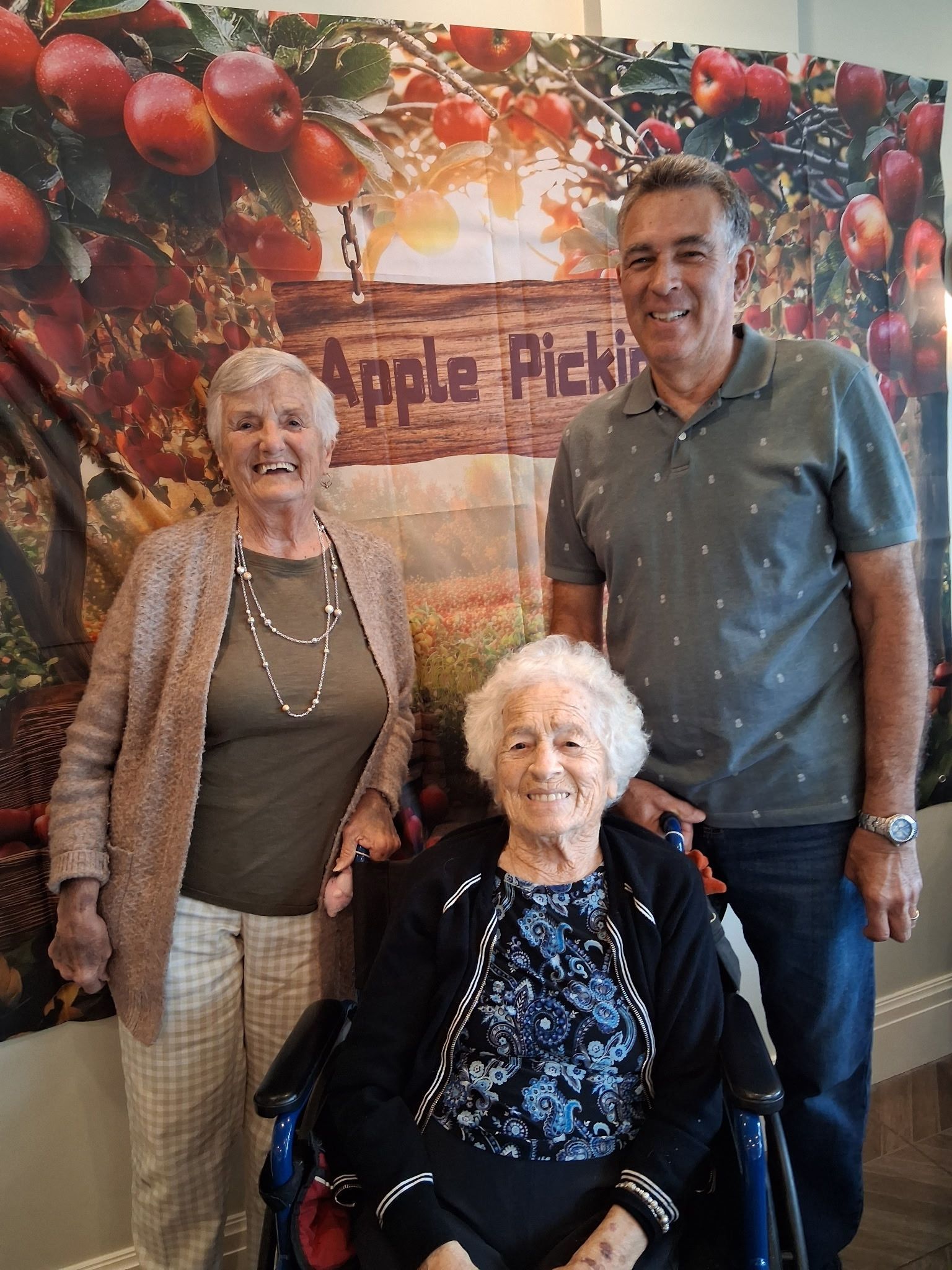 Three people posing in front of an Apple Picking banner with fruit decorations