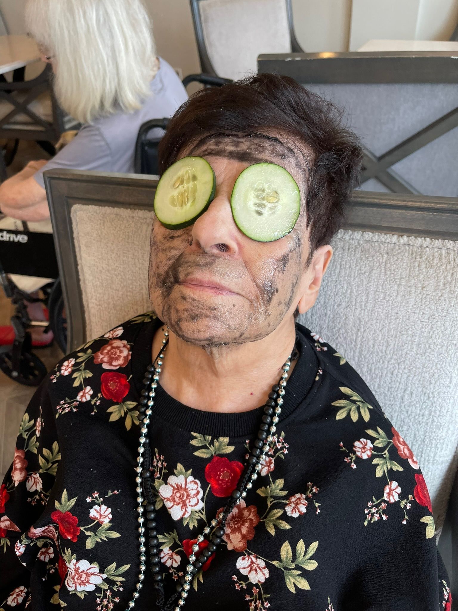 Woman with cucumber slices on eyes, facial mask, floral top, pearls.