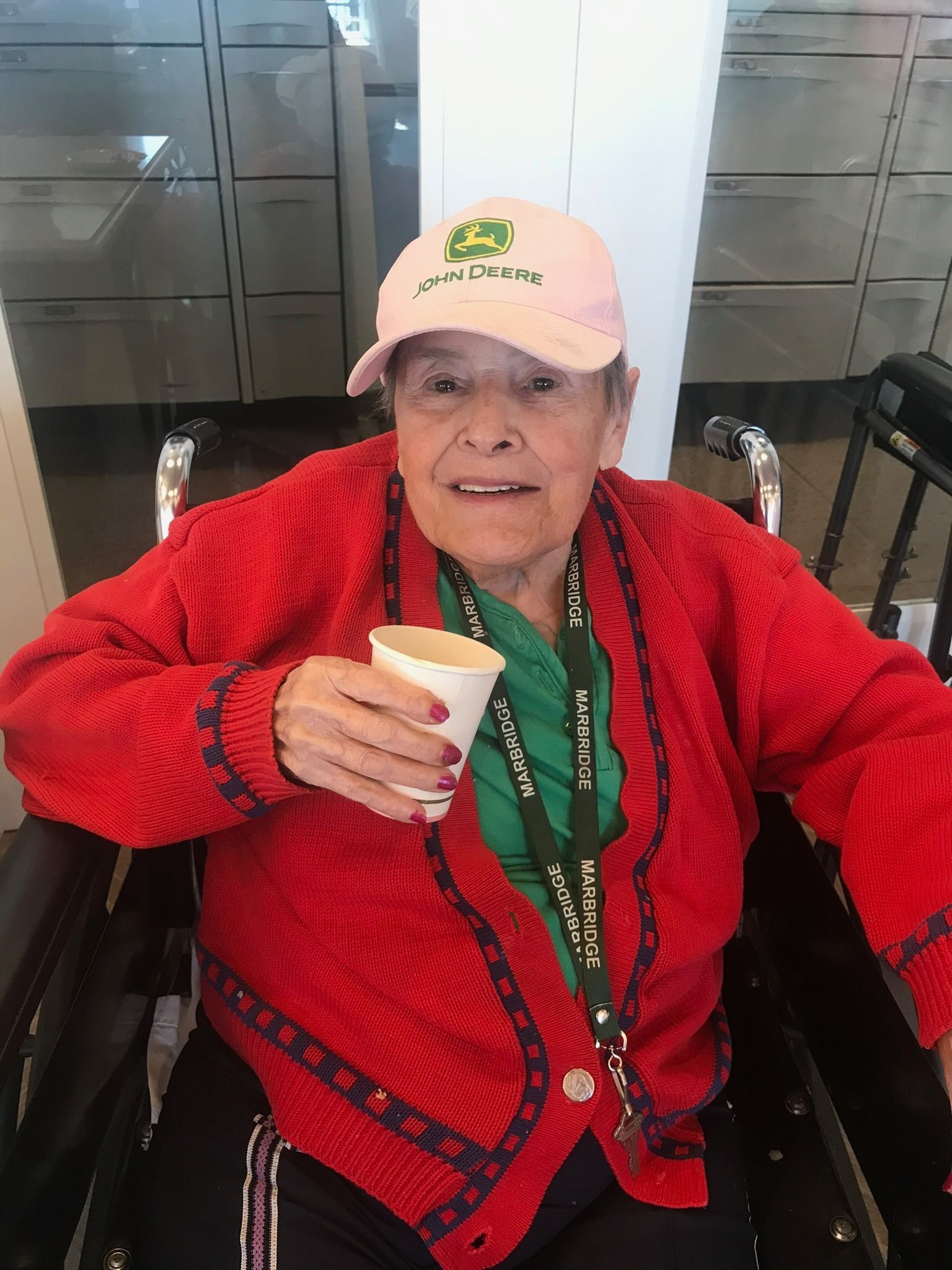 Woman in a wheelchair, holding a cup, wearing a pink hat and red sweater.