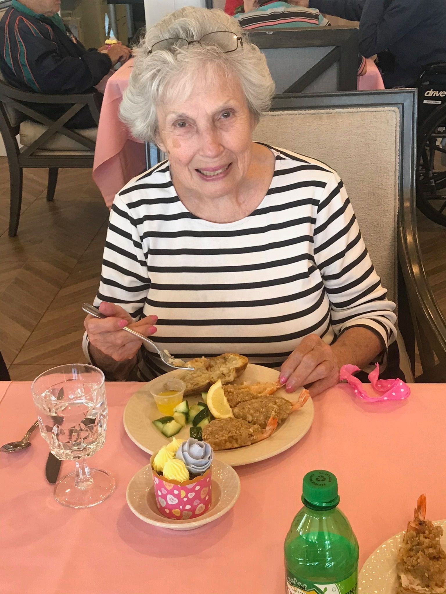 Woman in striped shirt eating meal at a table with a cupcake and drink.