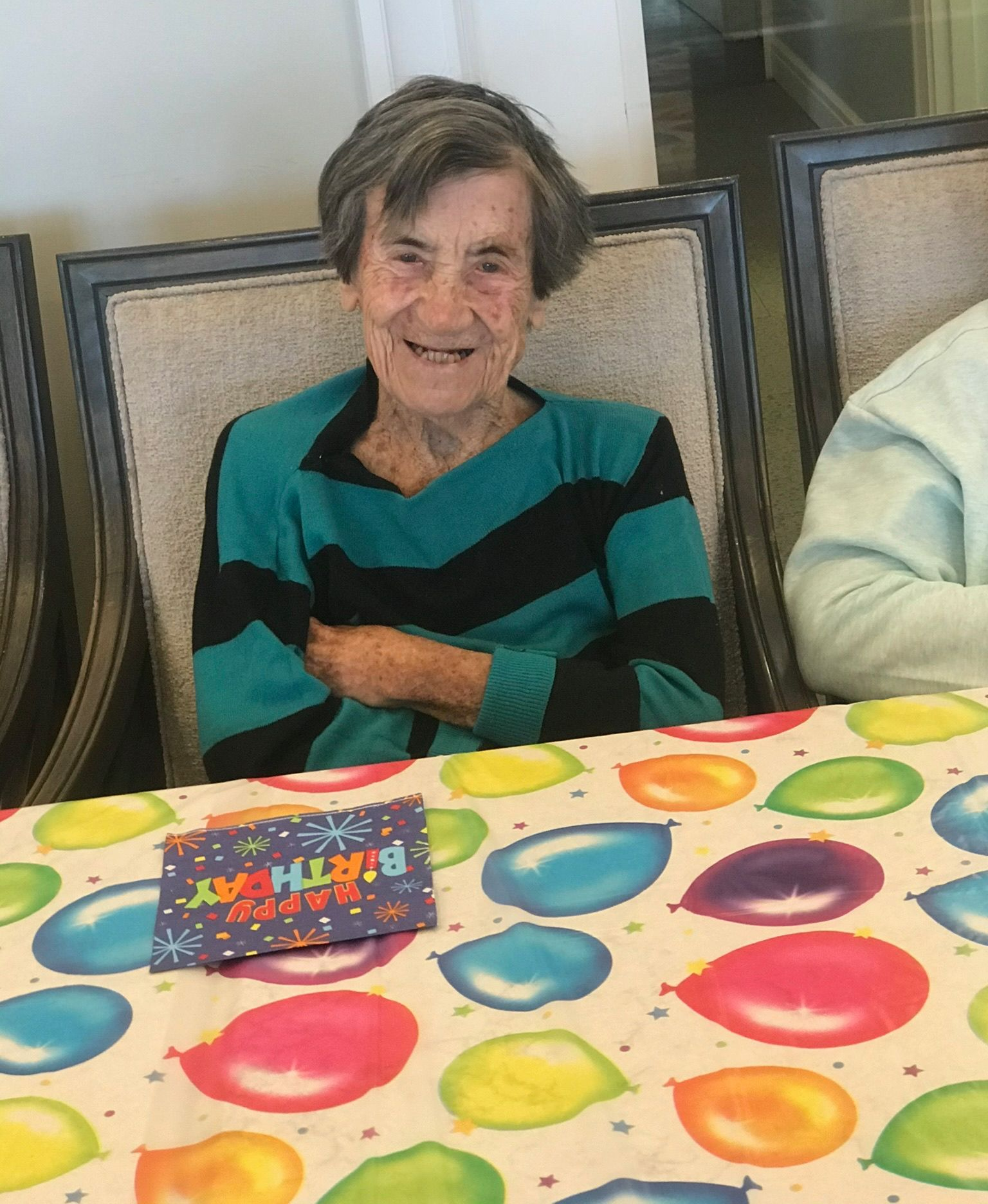 Woman sitting at a table with a birthday card, wearing a blue and black striped shirt, smiling.