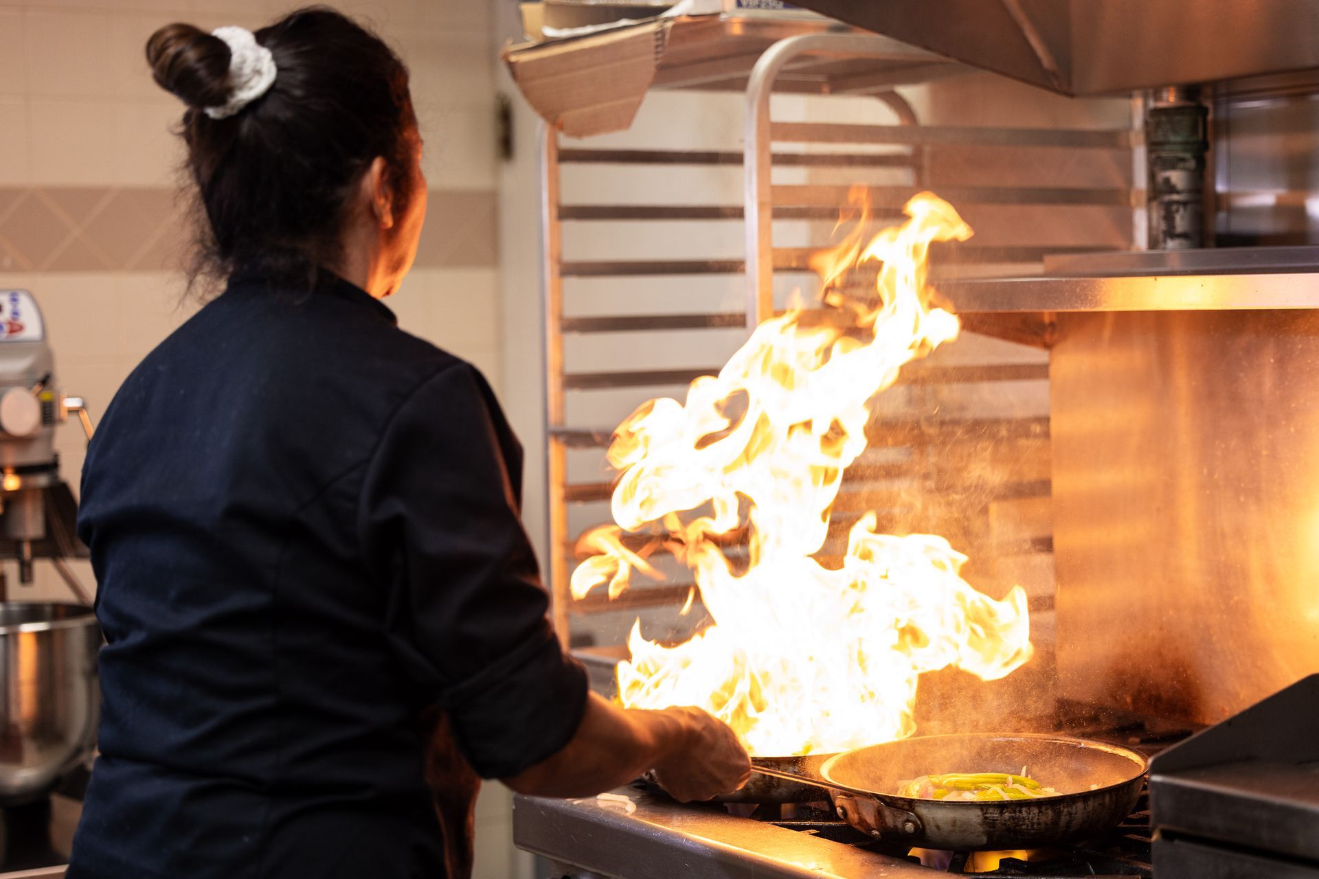 Woman cooking with flames in a kitchen.