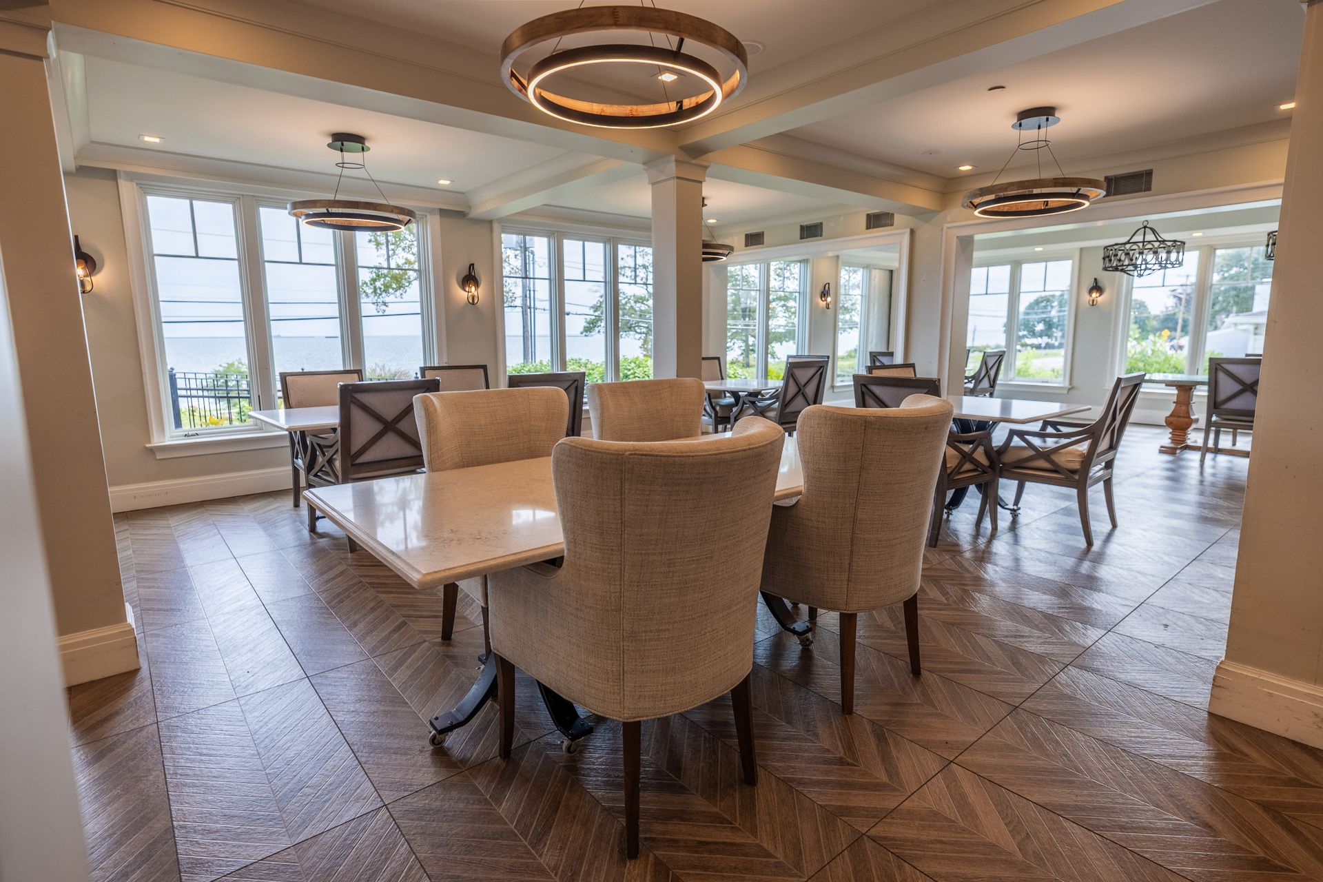 Dining room with tables, chairs, and large windows overlooking a waterfront view.