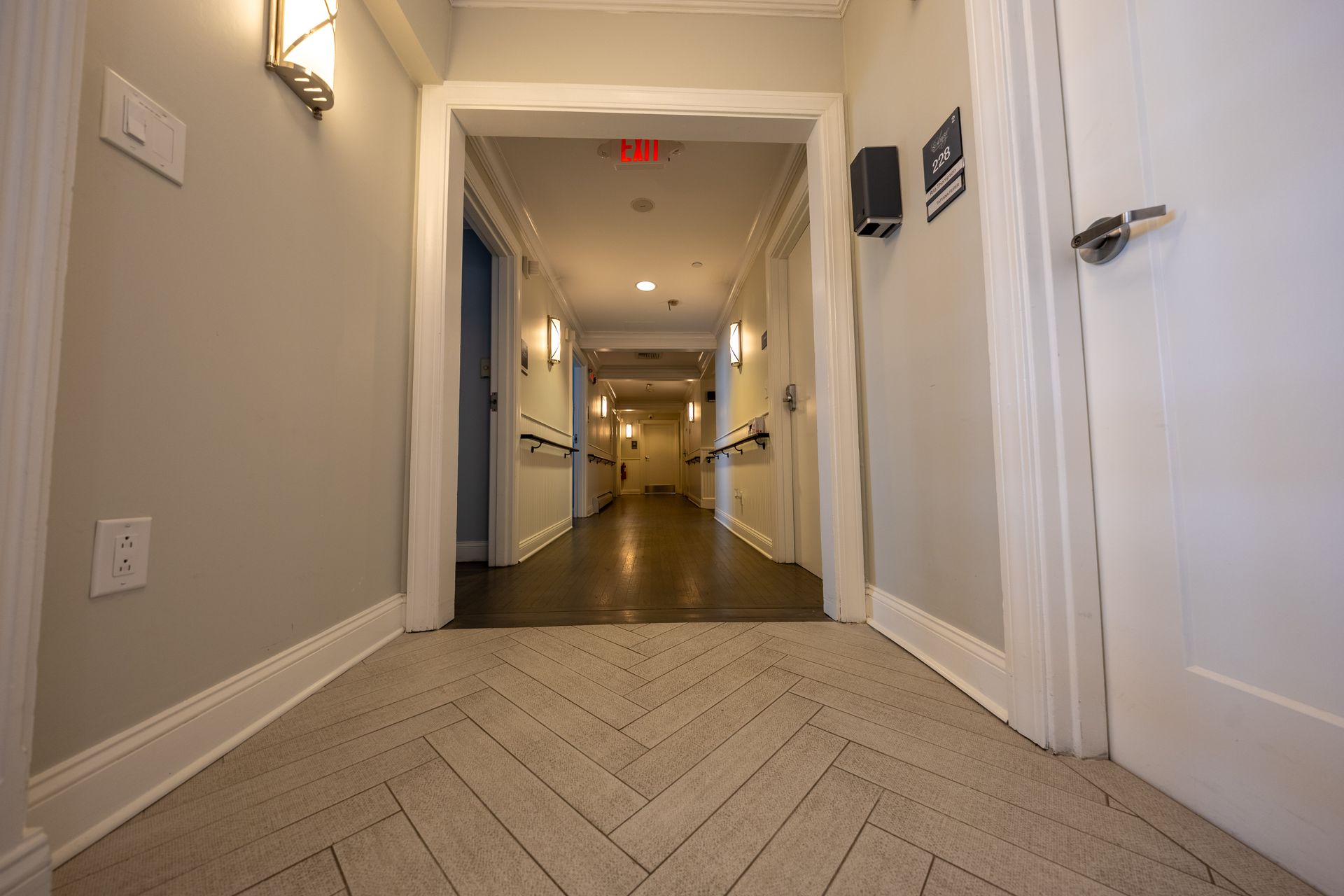 Long hallway with beige herringbone floor, white doors, and gray walls.