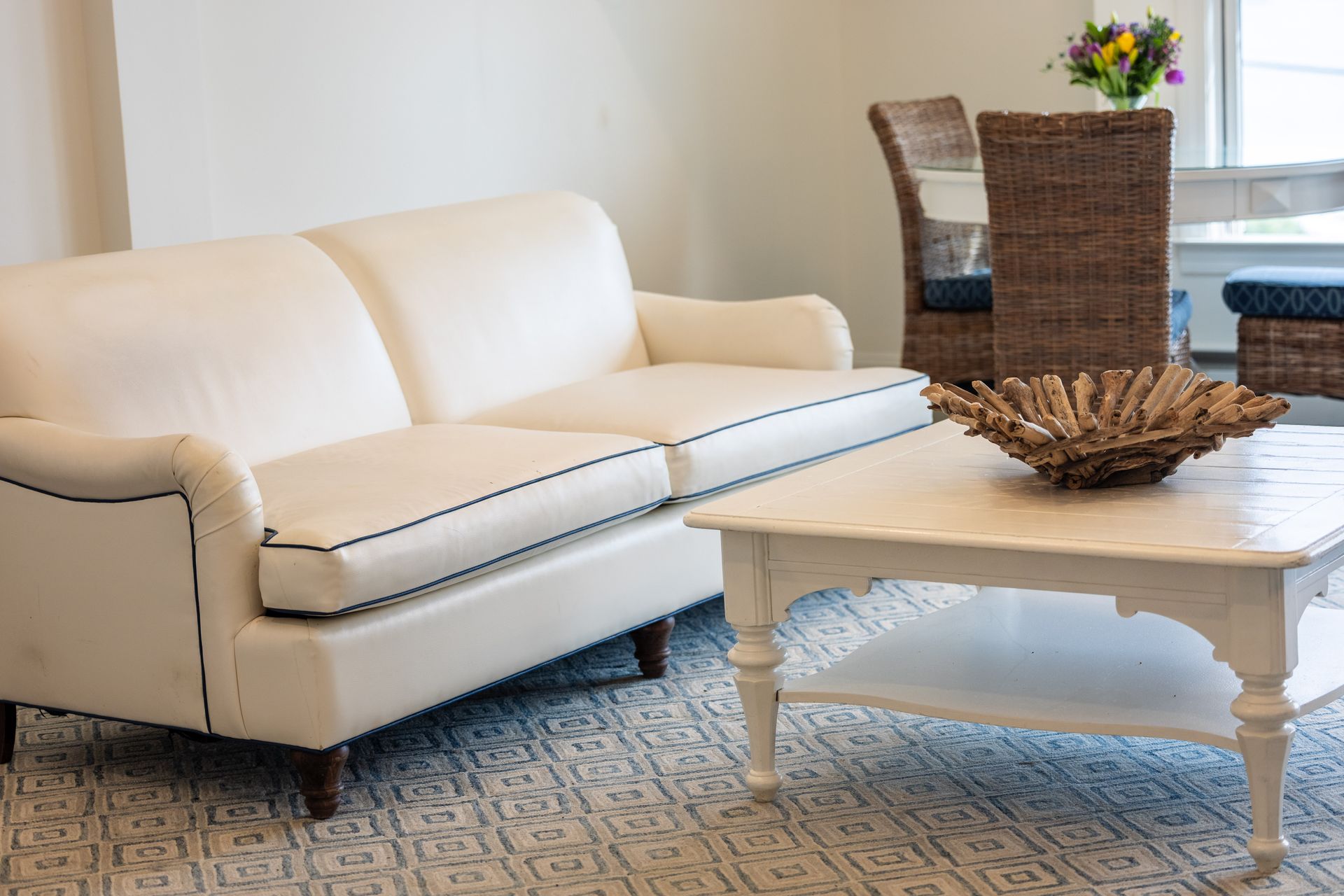 White sofa with navy trim, a white coffee table, and wicker chairs in a living room.