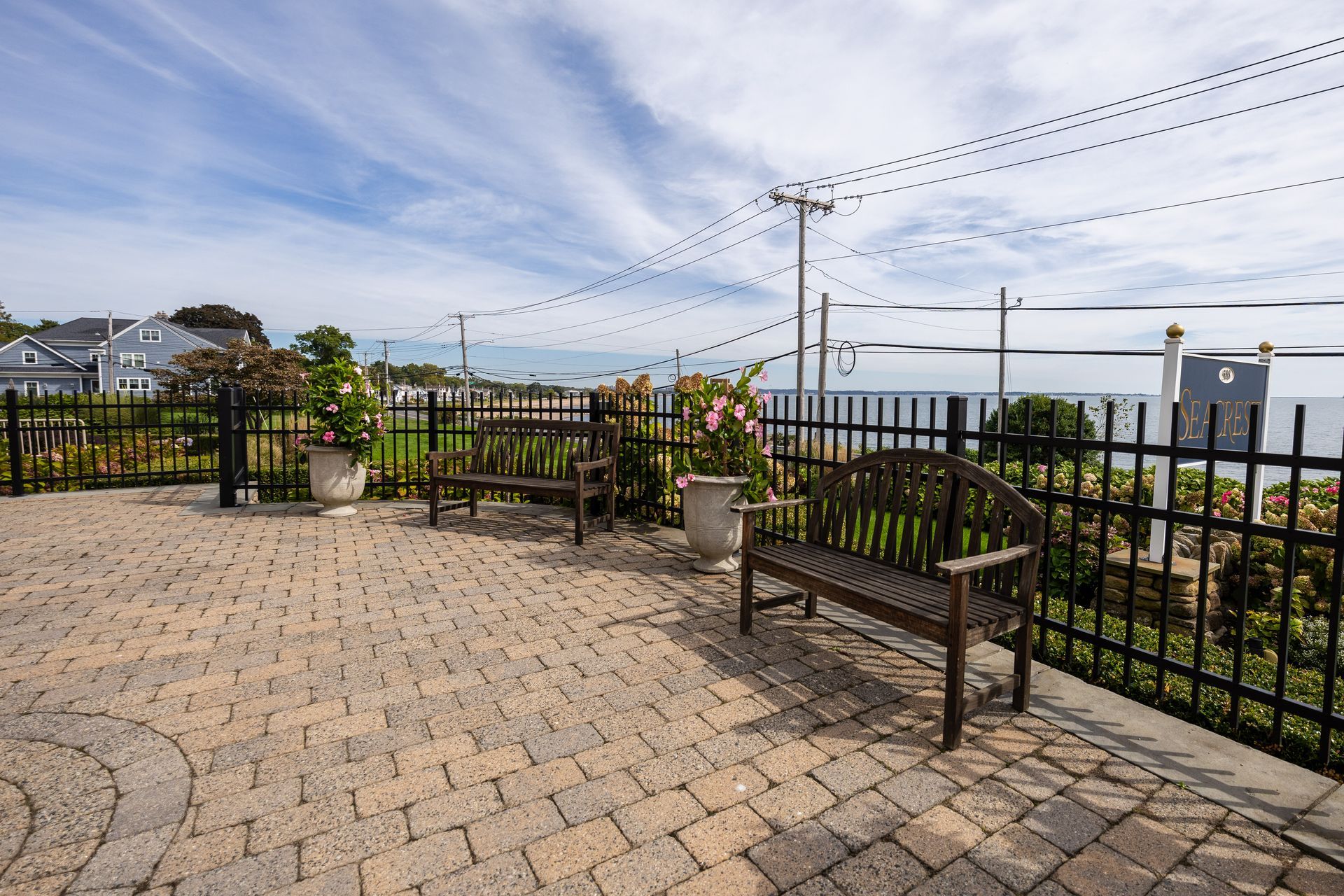Brick patio with benches, black fence, and view of the water under a cloudy sky.