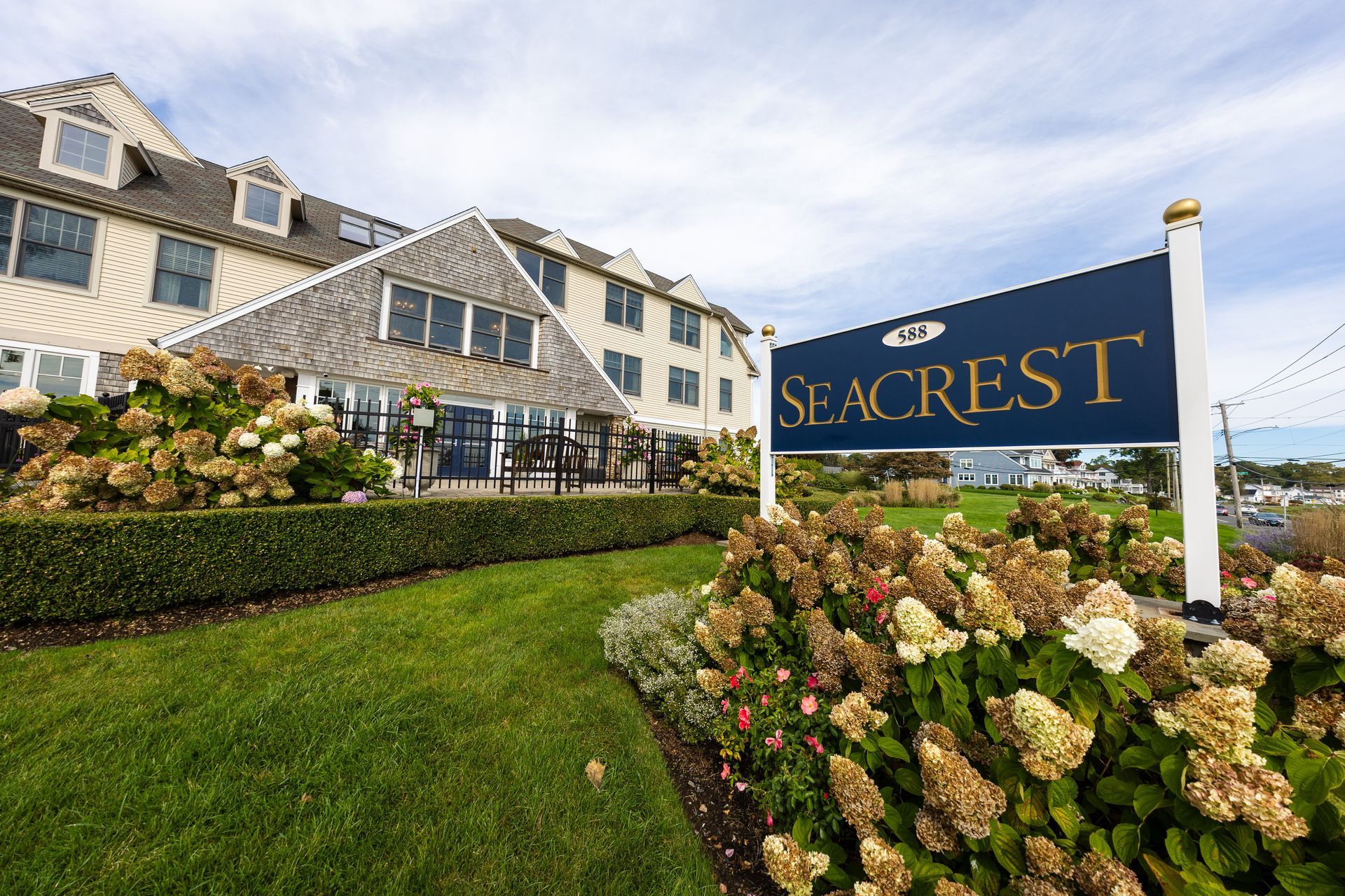 Seacrest hotel exterior with sign, green lawn, and beige building with multiple windows under a blue sky.
