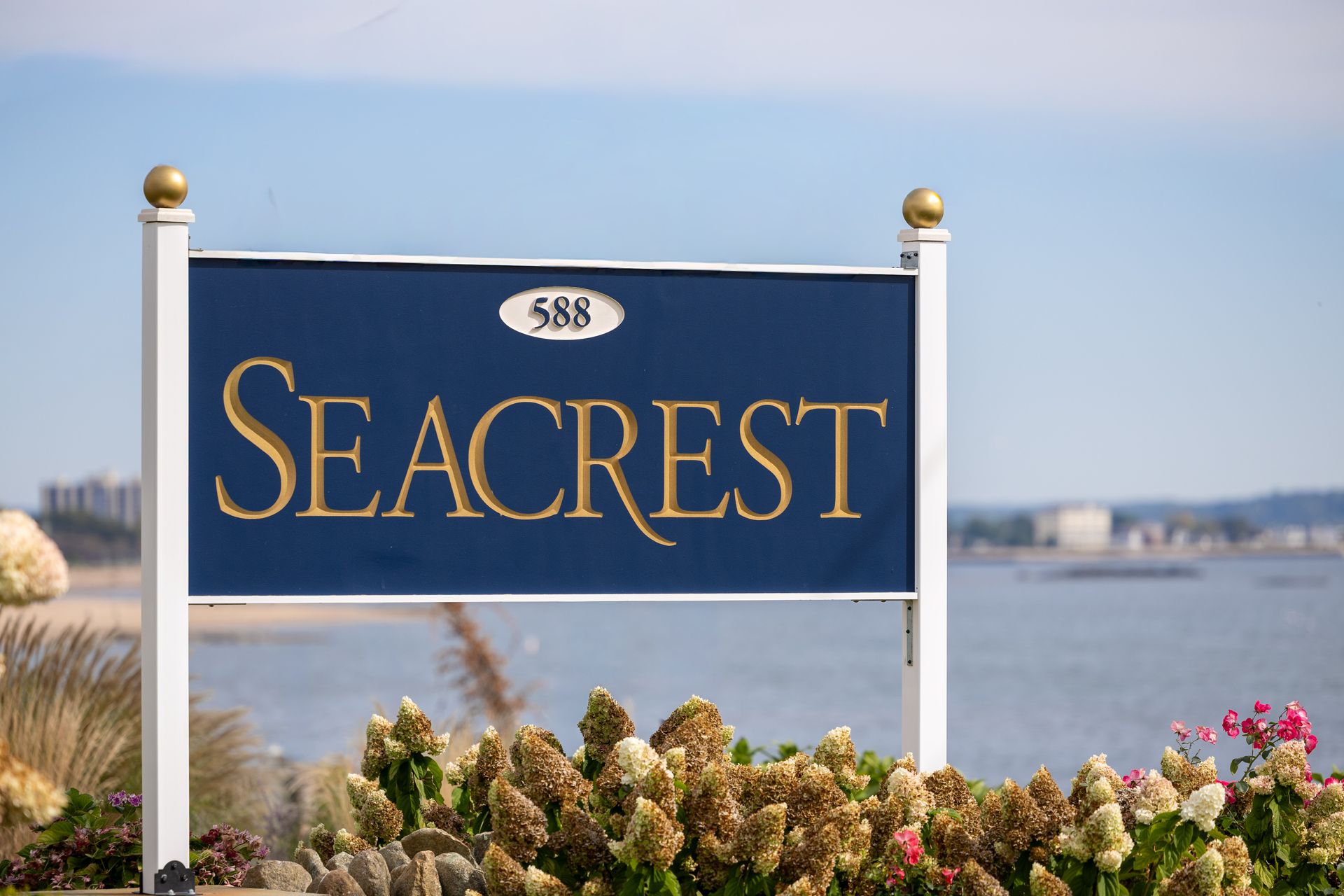 Sign for Seacrest apartment complex, blue with gold lettering, overlooking ocean.
