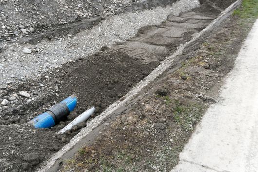 Un tubo blu giace nella terra vicino a un marciapiede.