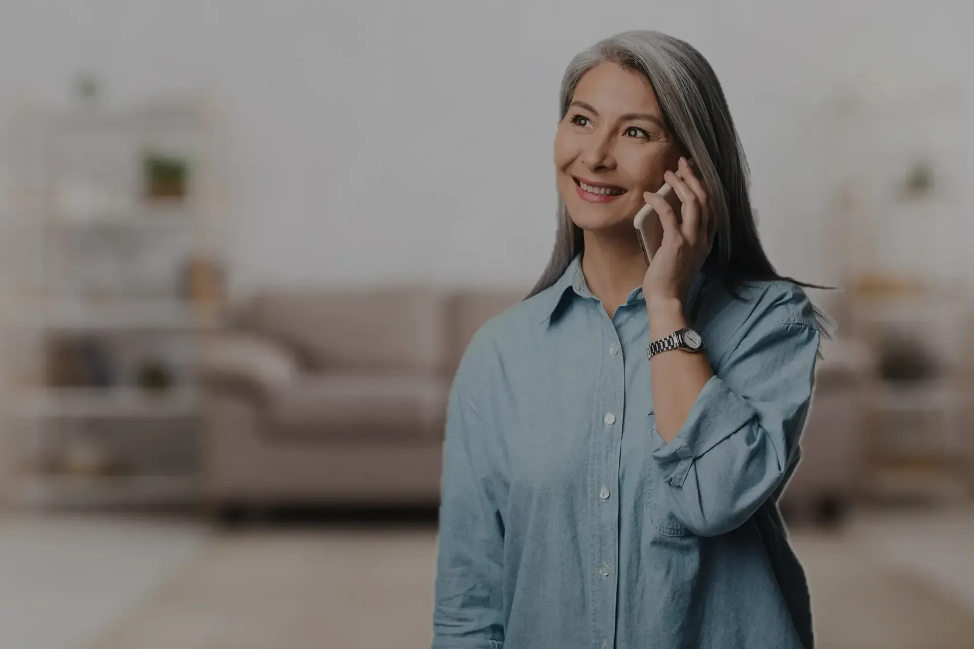 Smiling woman in a light blue shirt talking on a phone in a living room