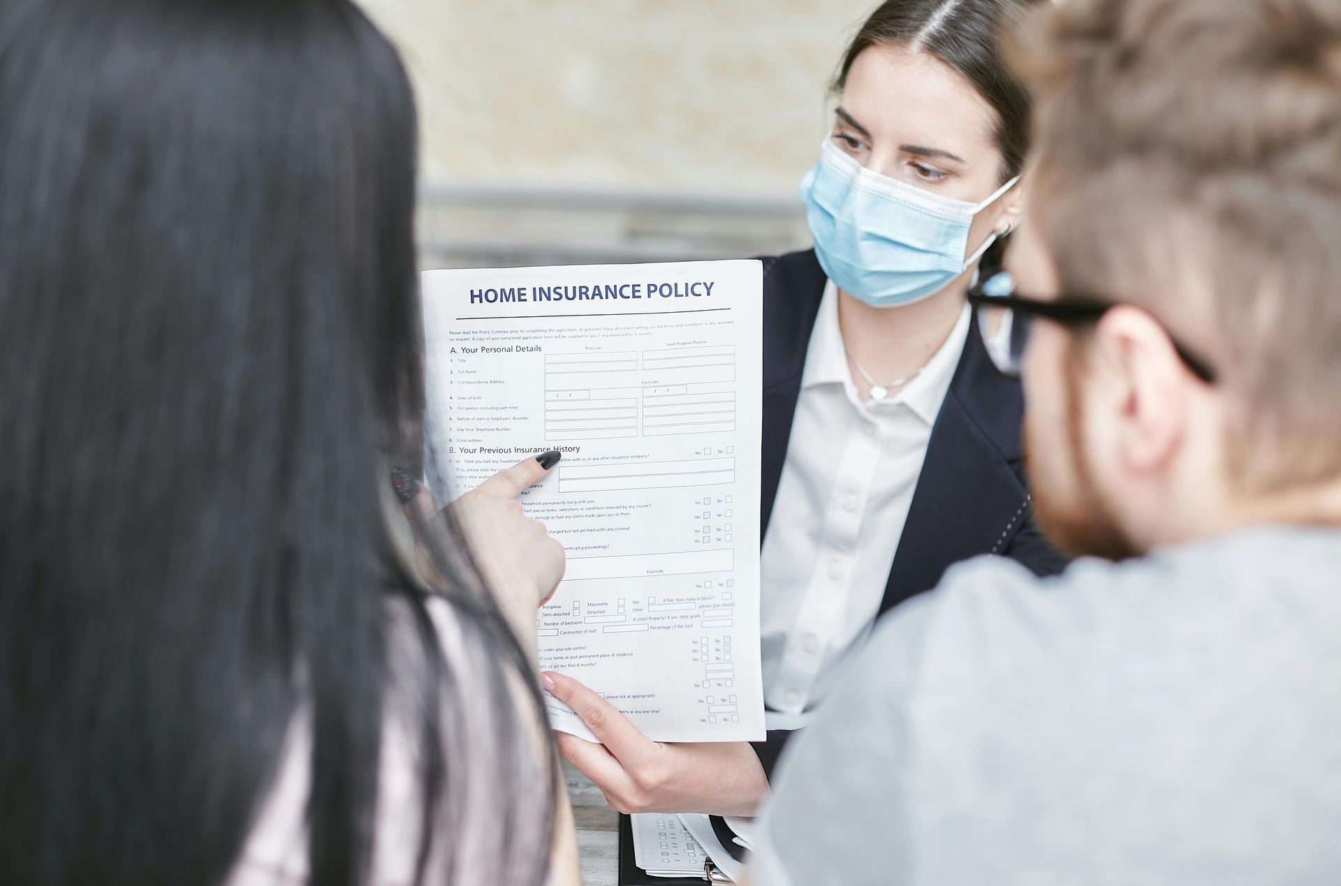 Woman in mask points to document for couple.