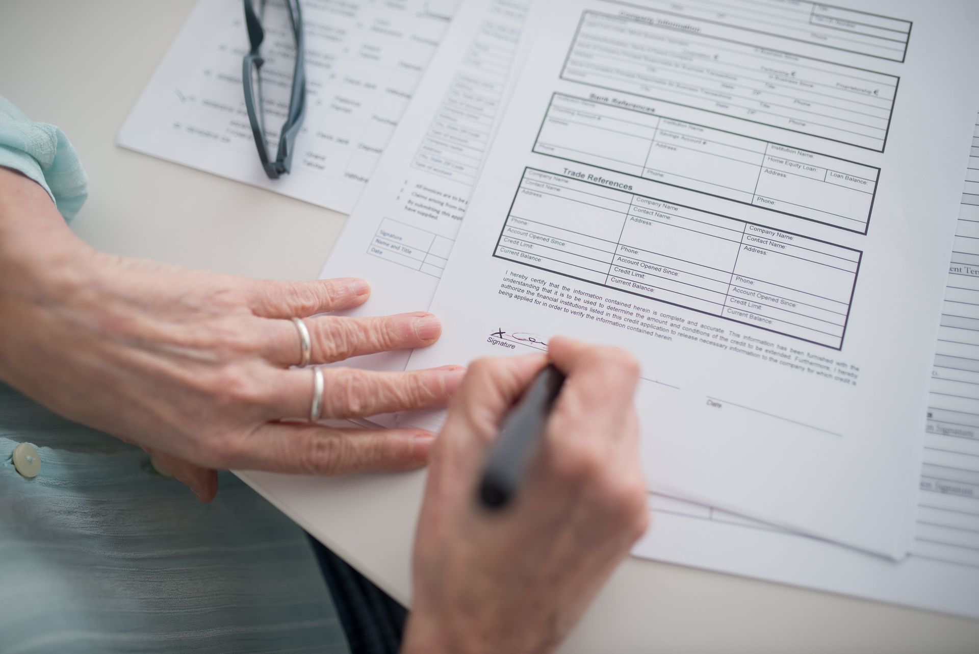 Hand filling out a form on a clipboard beside a stethoscope and paperwork