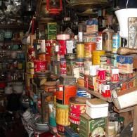A crowded shelf packed with various vintage food tins, containers, and household goods in a cluttered shop.