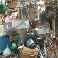 An assortment of vintage garden items, including metal funnels, buckets, and decorative accents, piled in an outdoor shop.