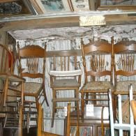 A row of wooden chairs, including a child's high chair, arranged in a display at an antique shop.