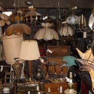 A cluttered antique shop display featuring various vintage hanging lamps, table lamps, and wooden furniture items.