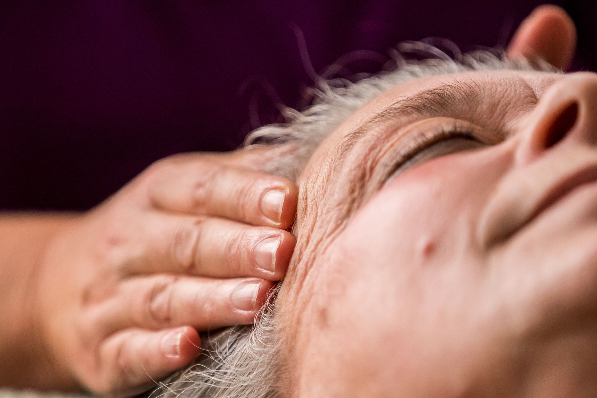 Hand masseert de slaap van een persoon met gesloten ogen; close-up.