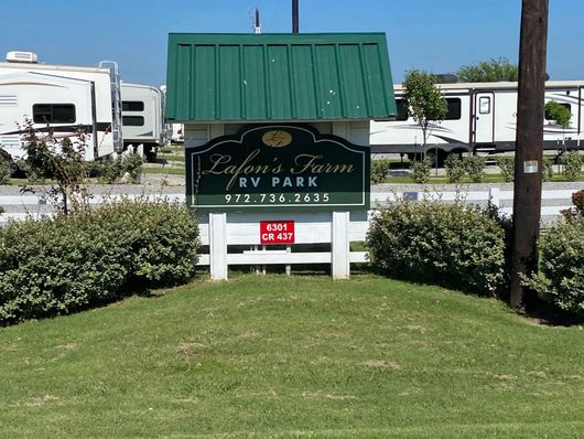 Sign for Lafon's Farm RV Park with green roof, surrounded by green bushes and parked RVs in the background.