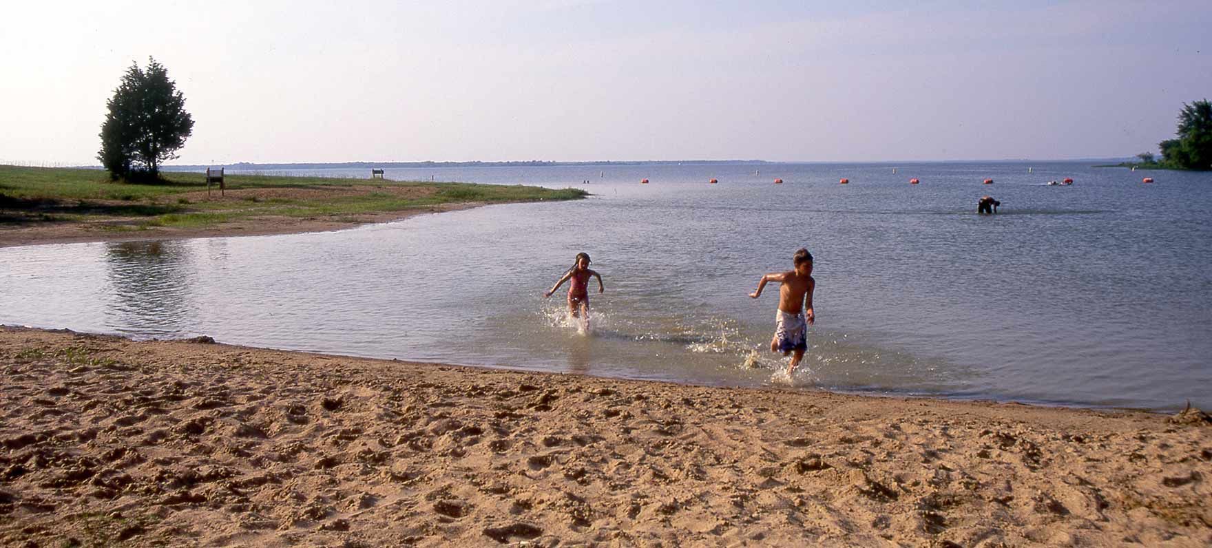 Two children running through water on a sandy beach in Lake Tawakoni State Park