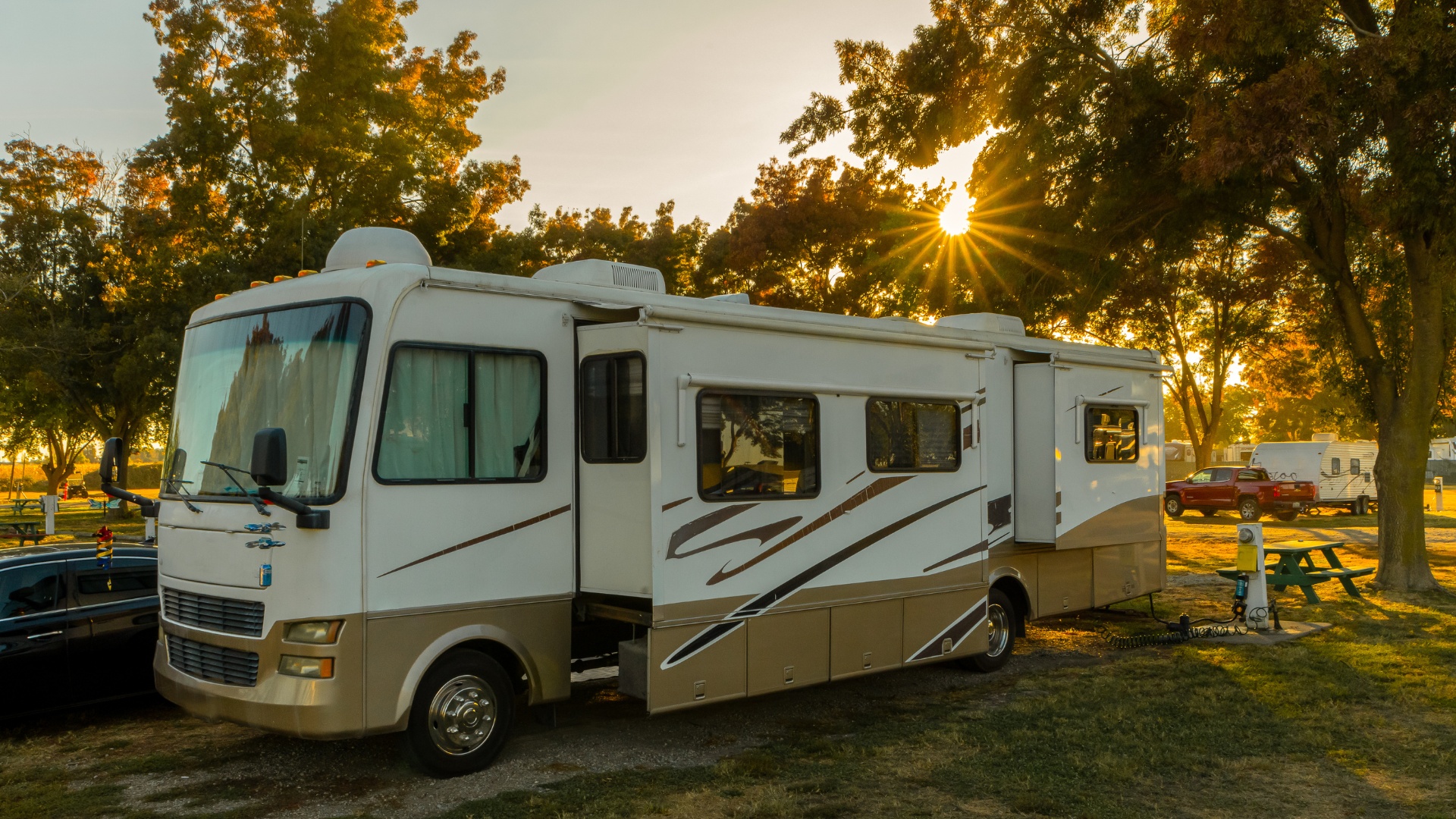 A rv is parked in a campground with the sun shining through the trees.