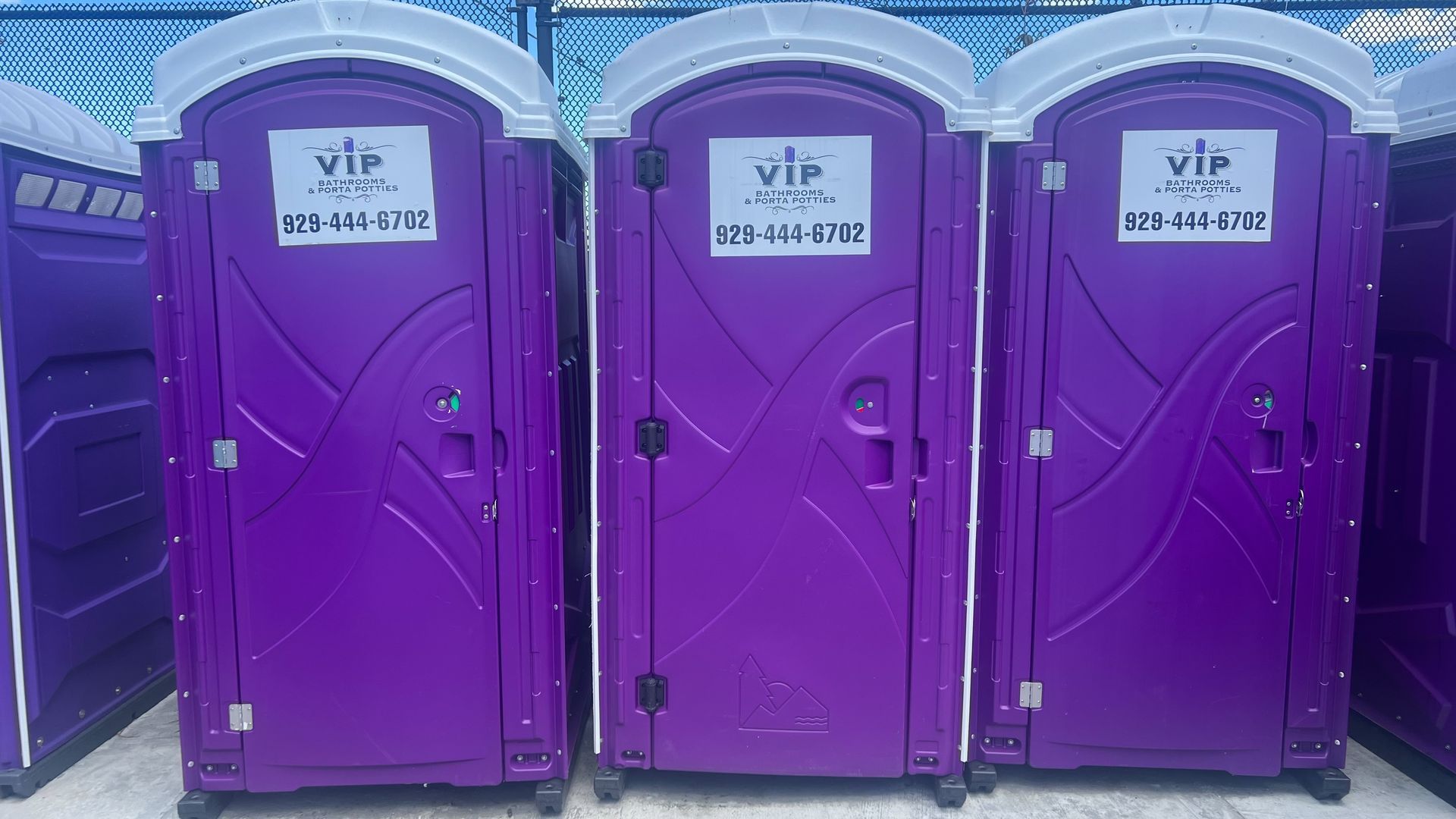 Three purple portable toilets lined up outdoors against a purple background.