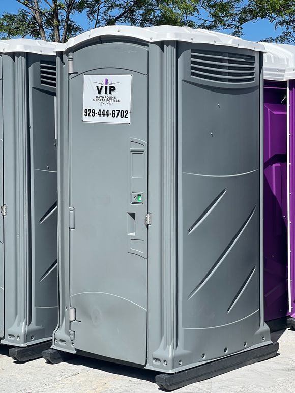 Gray portable toilet with a VIP sign, standing outdoors beside another unit.
