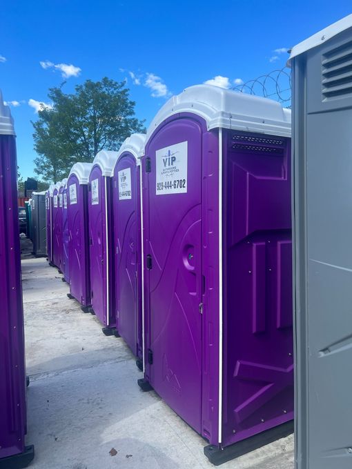 Row of purple portable toilets outdoors on a sunny day, with a gray unit in the foreground