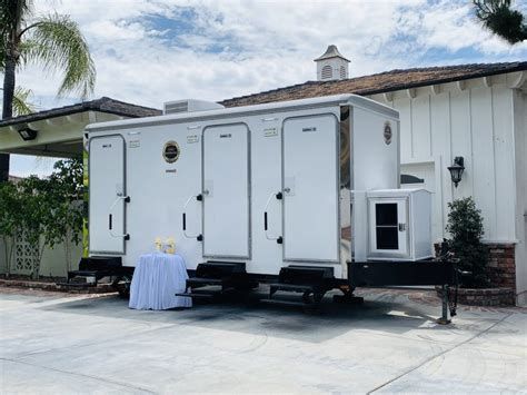 White mobile restroom trailer with steps and a small table outside a house driveway