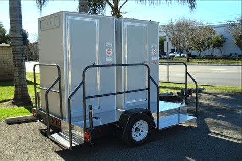 Portable restroom trailer with black railings parked outdoors on a sunny day